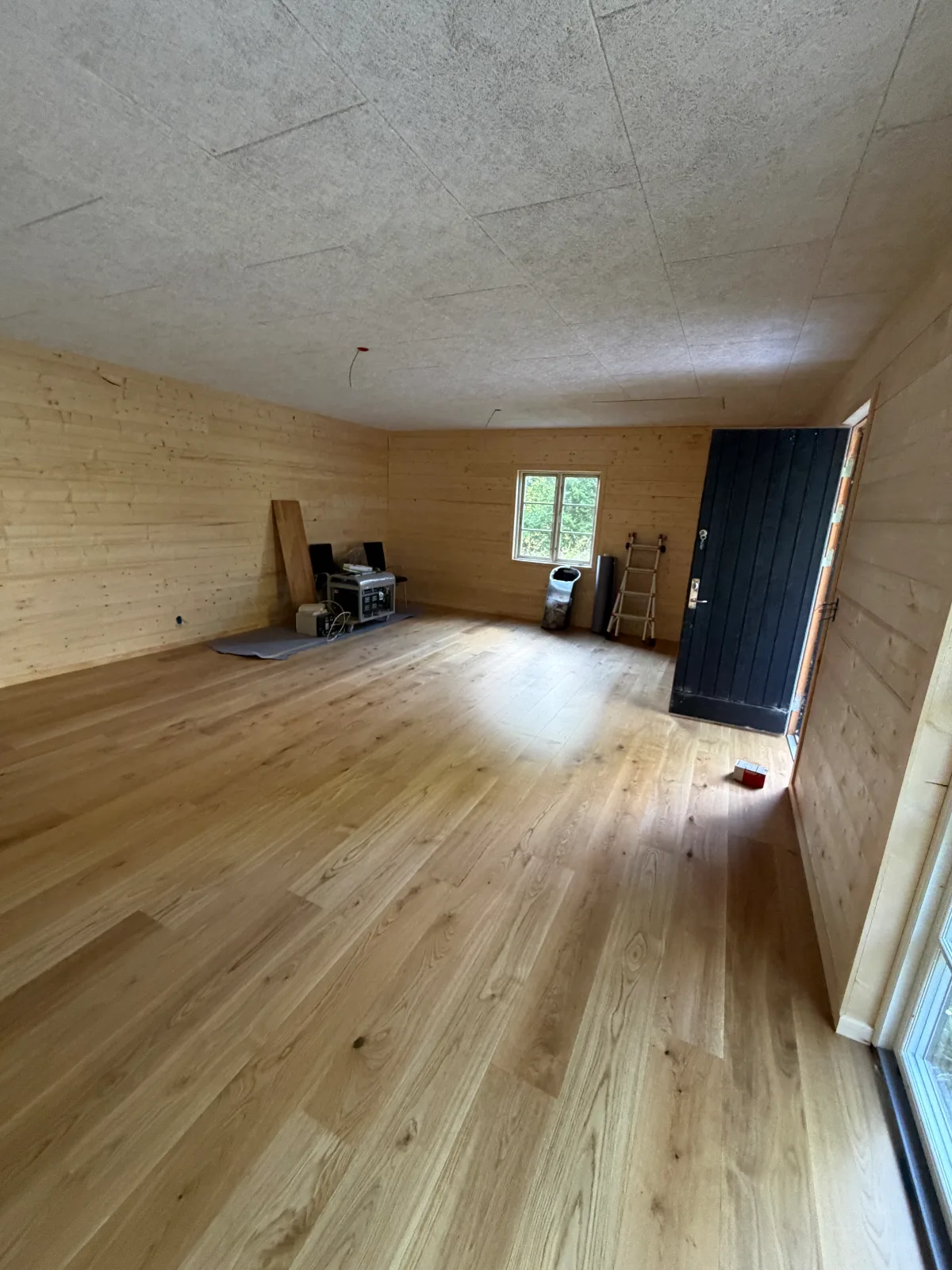 Nylagt egetræsgulv i et træbeklædt rum med pladebeklædt loft og ny yderdør